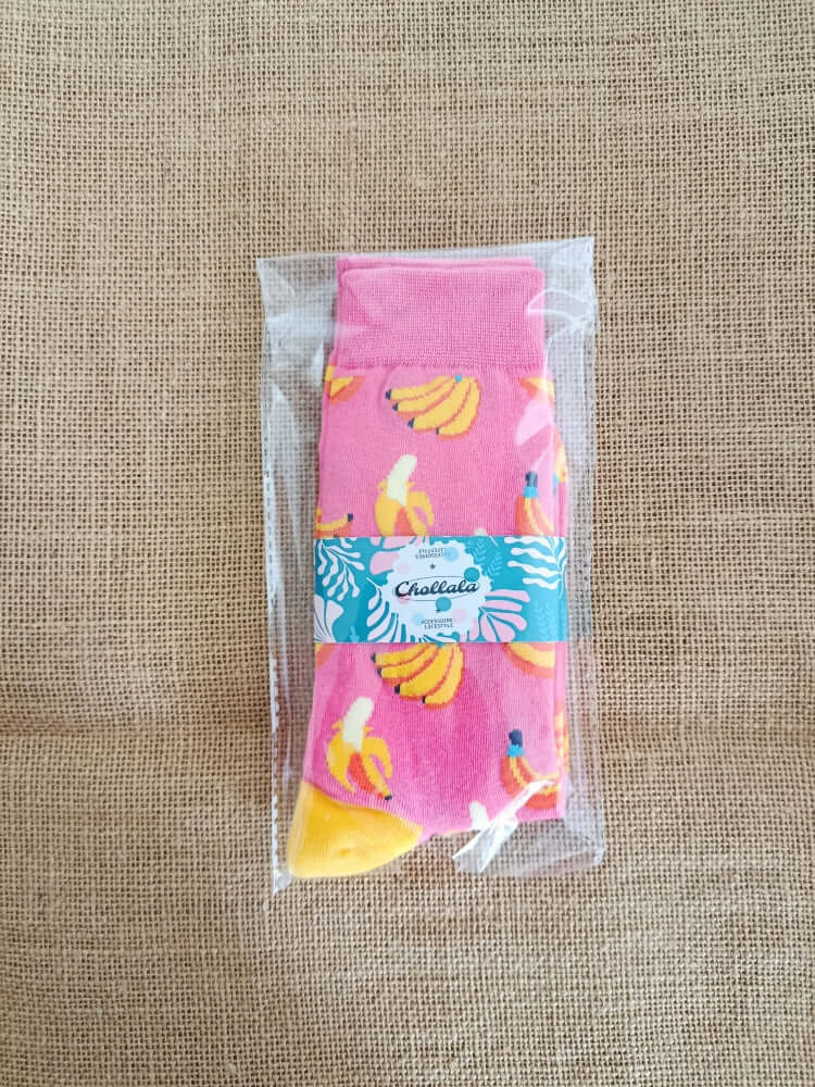 Chaussettes à motif banane coloré dans un emballage transparent, mettant en avant un design ludique sur fond rose.