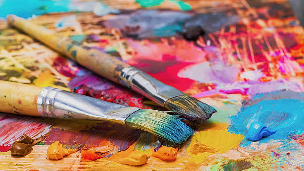 Deux pinceaux posés sur une palette recouverte de peinture colorée, symbolisant l’univers artistique de la collection de chaussettes Chollala.